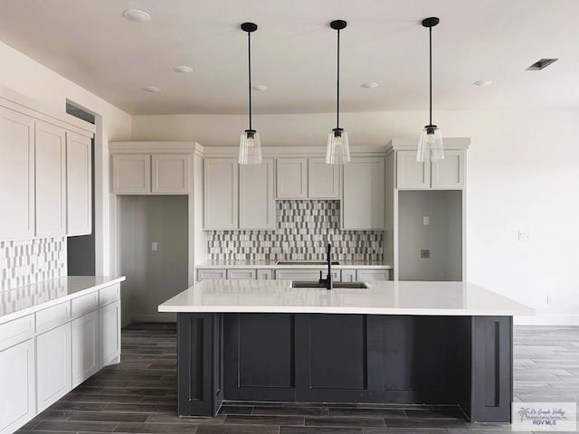 kitchen featuring decorative light fixtures, a kitchen island with sink, dark wood-type flooring, and sink