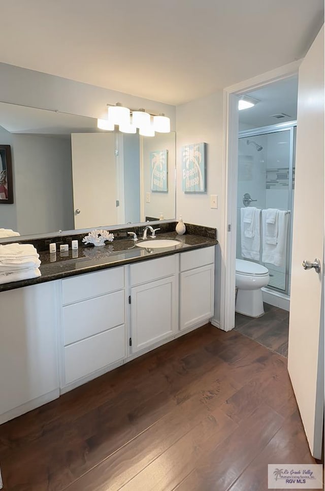 bathroom featuring vanity, toilet, wood-type flooring, and a shower with door