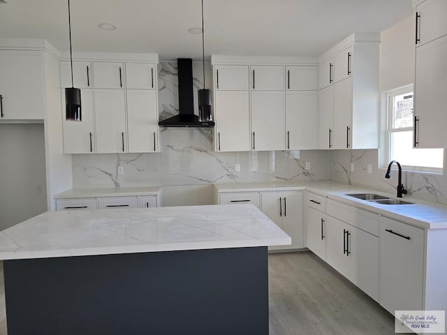 kitchen with decorative light fixtures, a kitchen island, wall chimney range hood, and sink