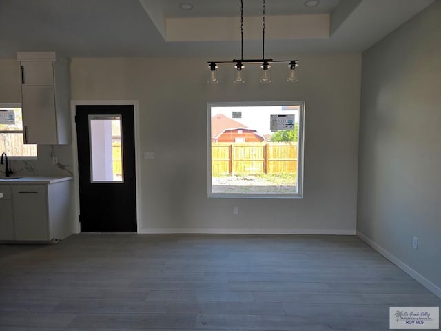 unfurnished dining area with sink, a tray ceiling, and light hardwood / wood-style flooring