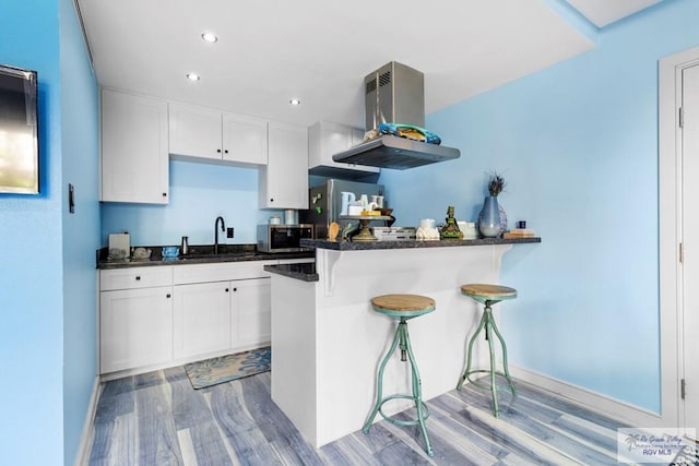 kitchen featuring a sink, light wood-style floors, island exhaust hood, a kitchen breakfast bar, and appliances with stainless steel finishes