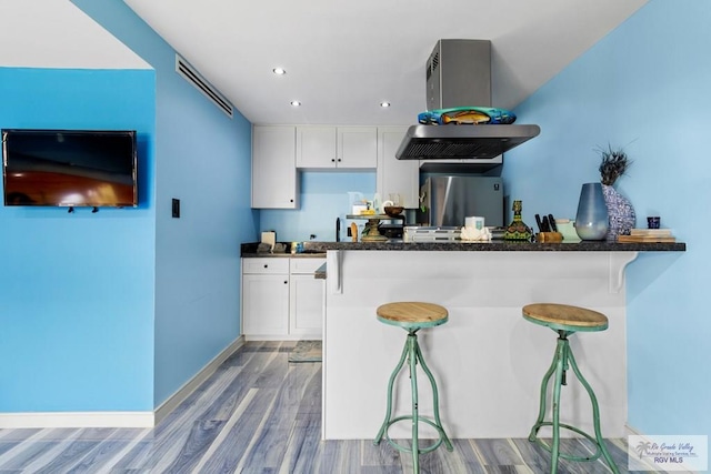 kitchen with wood finished floors, white cabinetry, freestanding refrigerator, a breakfast bar area, and baseboards