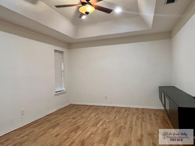 empty room featuring ceiling fan, light wood-type flooring, and a tray ceiling