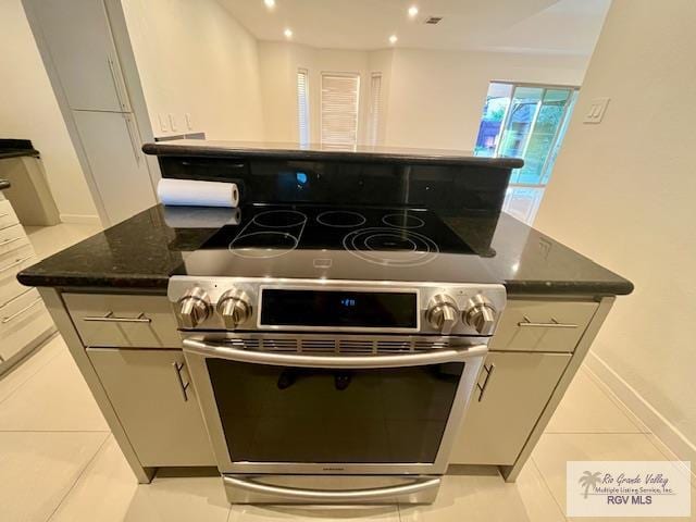 kitchen featuring light tile patterned flooring, gray cabinetry, stainless steel range with electric stovetop, a kitchen island, and dark stone counters