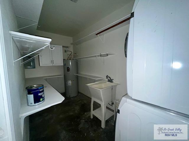 laundry area featuring stacked washing maching and dryer, electric water heater, and sink