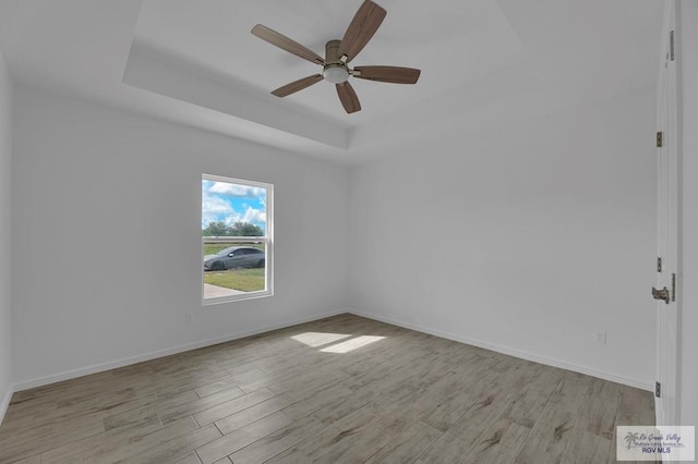 empty room with a tray ceiling, ceiling fan, and light hardwood / wood-style flooring