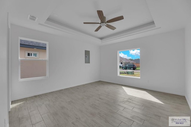 empty room featuring a tray ceiling, electric panel, ceiling fan, and light hardwood / wood-style floors