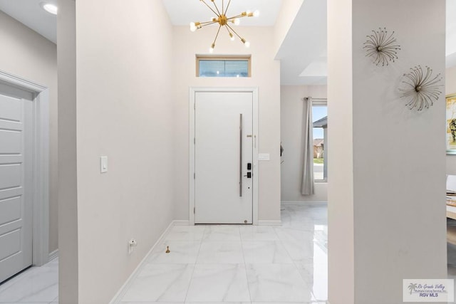 entrance foyer featuring a chandelier, marble finish floor, and baseboards