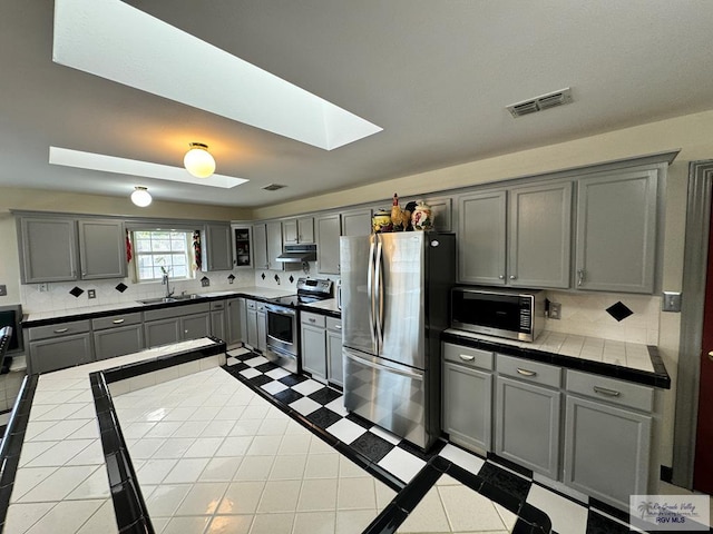 kitchen with tile counters, gray cabinets, stainless steel appliances, and a skylight