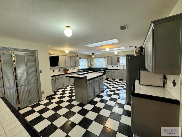 kitchen with gray cabinetry, a skylight, a center island, sink, and backsplash