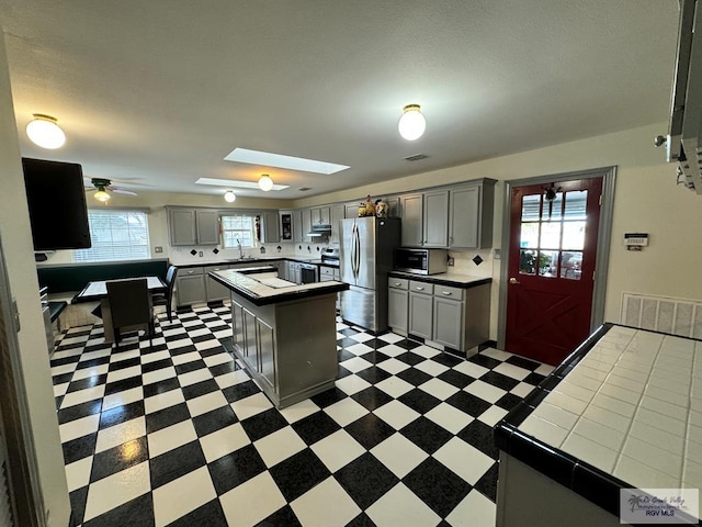 kitchen featuring gray cabinetry, a center island, a skylight, ceiling fan, and stainless steel appliances