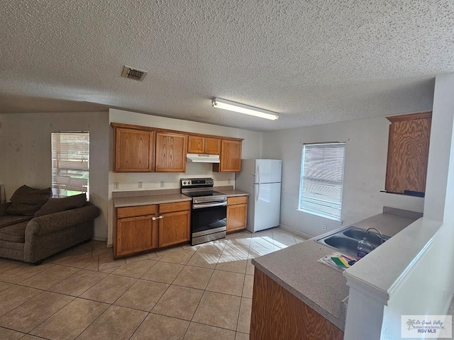 1149 Champlain Dr, Brownsville, TX 78526 - kitchen with stainless steel electric range, a healthy amount of sunlight, white refrigerator, sink, and light tile patterned flooring