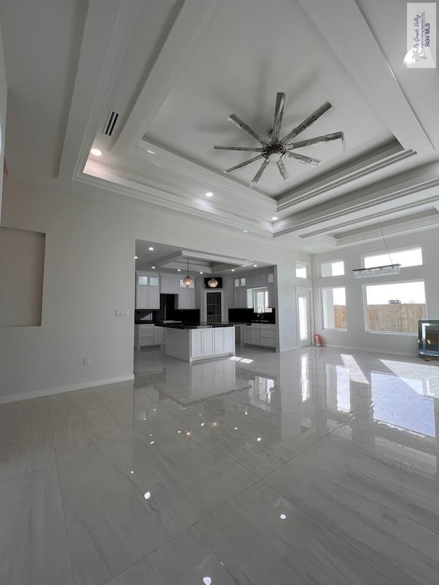 unfurnished living room with visible vents, a ceiling fan, baseboards, marble finish floor, and a raised ceiling