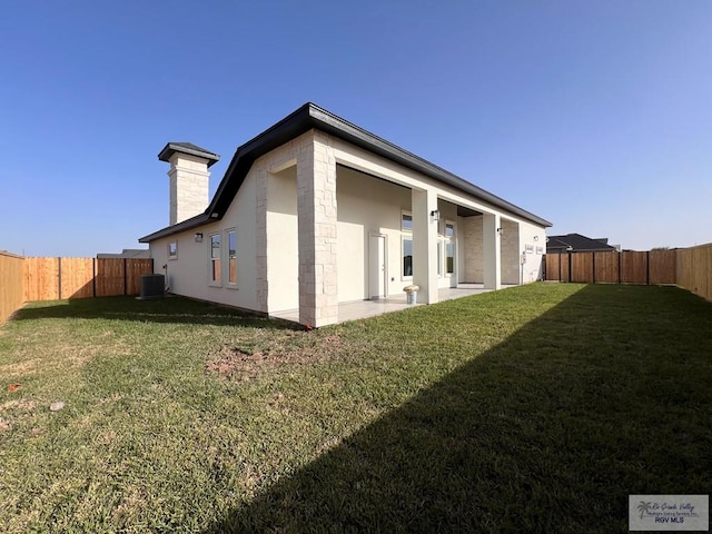 back of property featuring a fenced backyard, a lawn, a chimney, and central AC unit