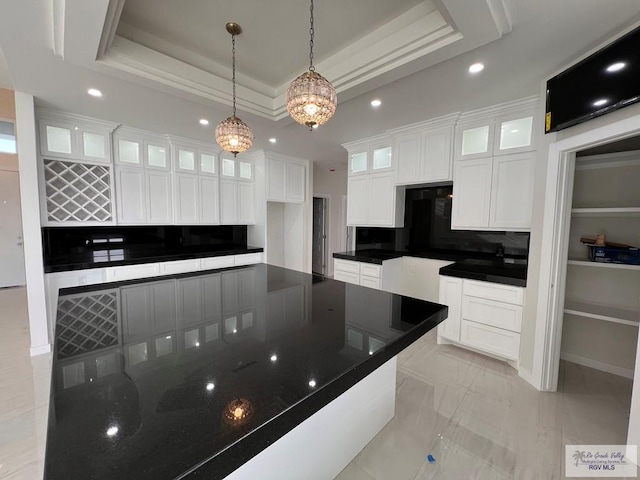 kitchen with a tray ceiling, pendant lighting, dark countertops, decorative backsplash, and white cabinetry