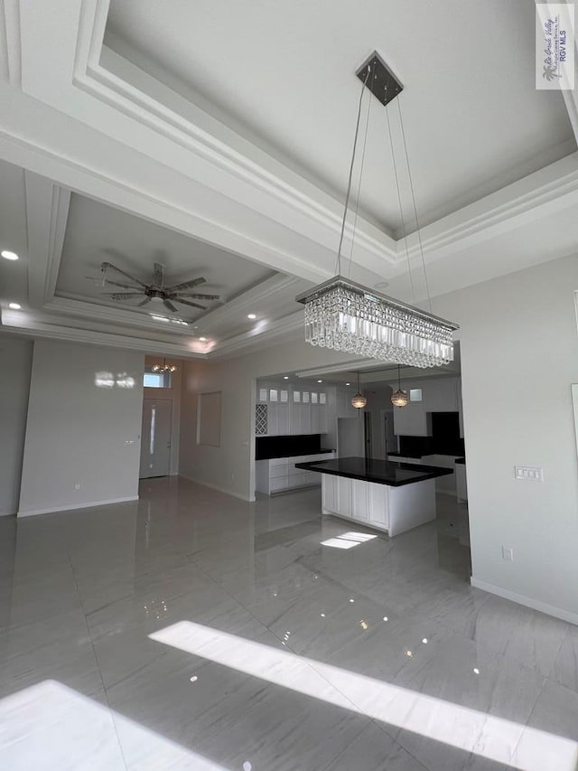 interior space with white cabinets, baseboards, a center island, dark countertops, and a raised ceiling