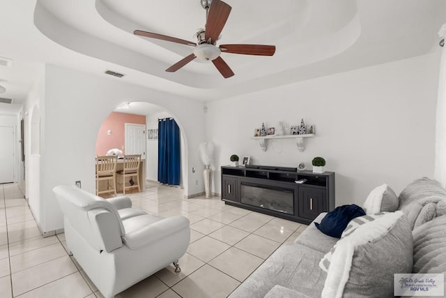 tiled living room with a tray ceiling and ceiling fan