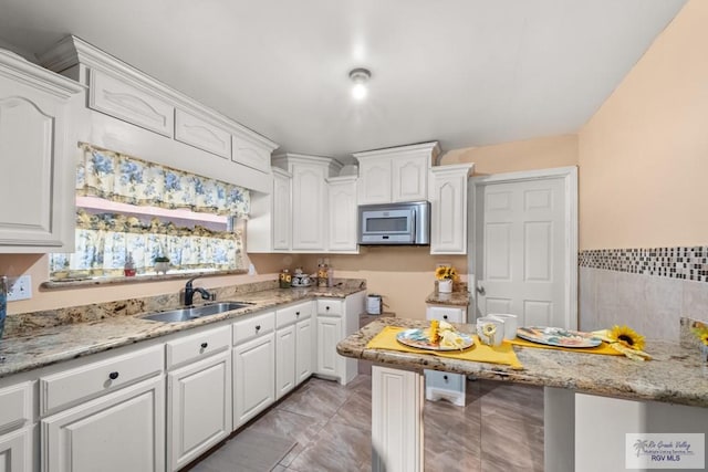 kitchen with white cabinetry, sink, light stone counters, and light tile patterned floors