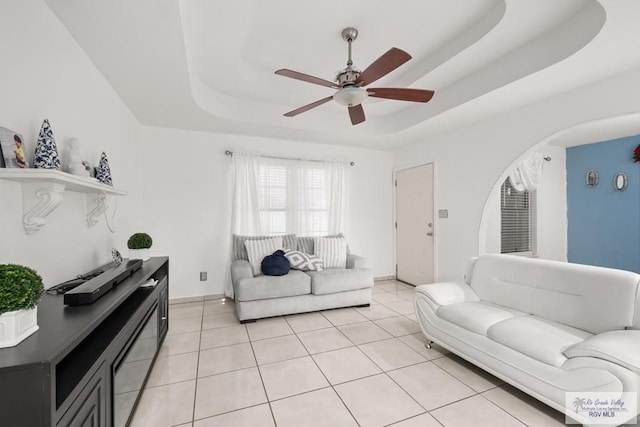 living room with light tile patterned floors, a tray ceiling, and ceiling fan