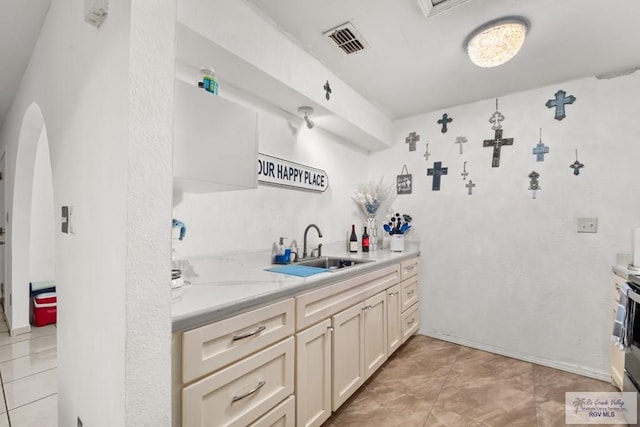 kitchen featuring sink, light tile patterned floors, light stone counters, cream cabinets, and stainless steel range with electric cooktop