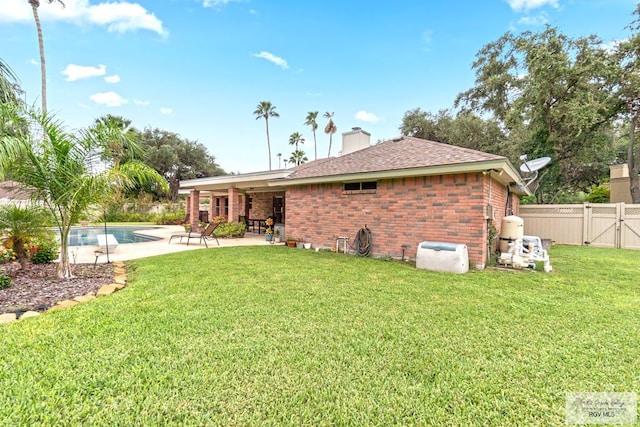 rear view of house with a fenced in pool, a patio area, and a lawn