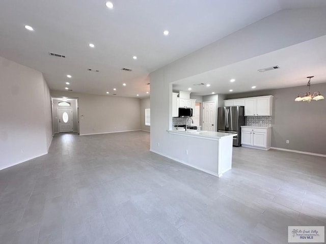 kitchen with backsplash, sink, stainless steel fridge, white cabinetry, and a chandelier