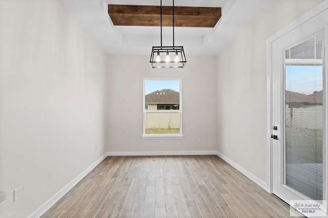 unfurnished dining area featuring a tray ceiling and light hardwood / wood-style floors