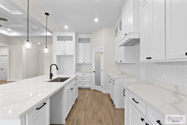 kitchen with light stone countertops, white cabinetry, sink, pendant lighting, and light wood-type flooring