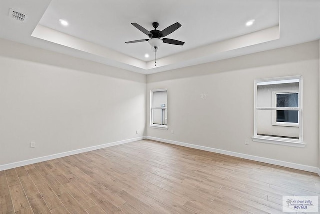 empty room featuring a raised ceiling, ceiling fan, and light wood-type flooring