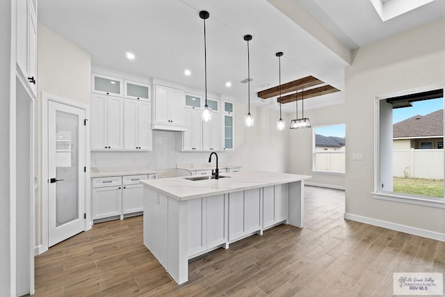 kitchen featuring a kitchen island with sink, white cabinets, sink, light stone countertops, and decorative light fixtures