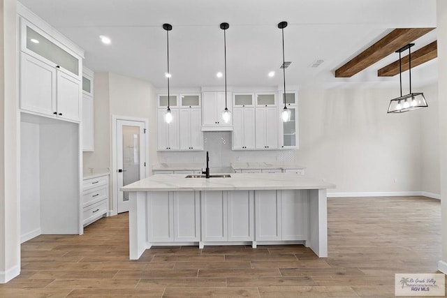 kitchen with white cabinets, beam ceiling, an island with sink, and sink