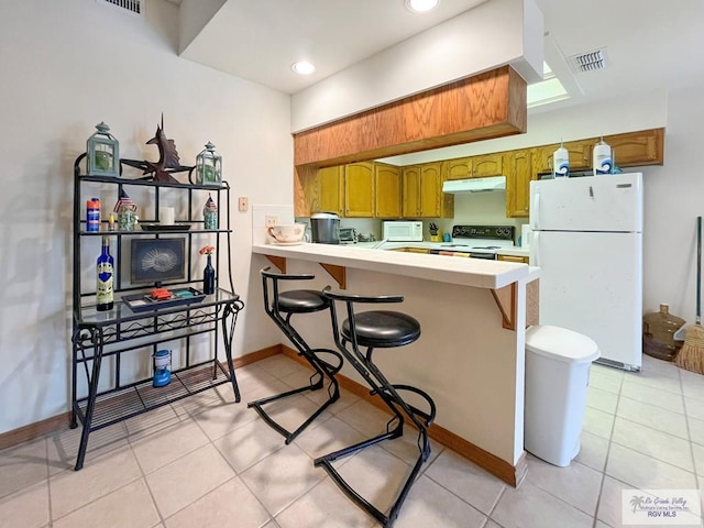 kitchen with light tile patterned floors, kitchen peninsula, white appliances, and a breakfast bar area