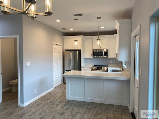 kitchen featuring white cabinetry, pendant lighting, stainless steel appliances, and wood-type flooring