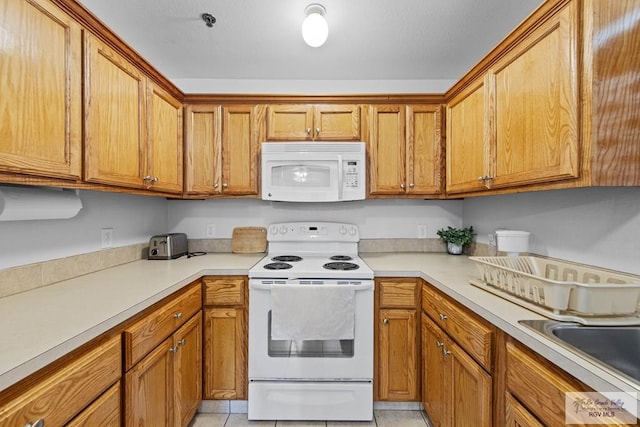 kitchen featuring sink, light tile patterned floors, and white appliances