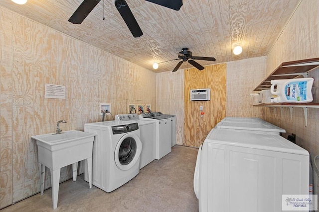 clothes washing area featuring ceiling fan, wood walls, washing machine and dryer, and sink