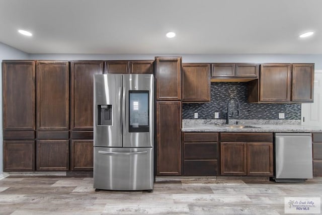 kitchen featuring sink, light stone counters, light hardwood / wood-style floors, stainless steel fridge with ice dispenser, and decorative backsplash