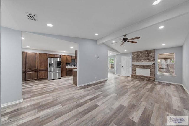 unfurnished living room with plenty of natural light, a fireplace, lofted ceiling with beams, and light wood-type flooring