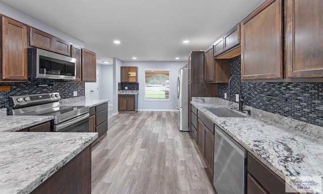 kitchen featuring sink, light hardwood / wood-style flooring, appliances with stainless steel finishes, light stone countertops, and backsplash