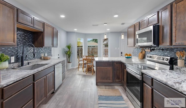 kitchen with appliances with stainless steel finishes, decorative light fixtures, sink, dark brown cabinetry, and light stone countertops