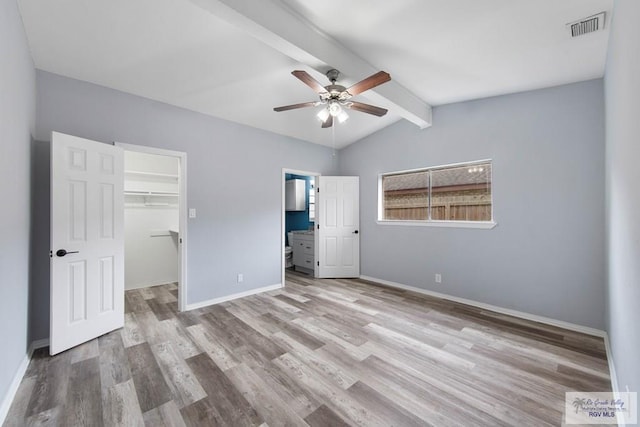 unfurnished bedroom with connected bathroom, light hardwood / wood-style floors, lofted ceiling with beams, a walk in closet, and a closet