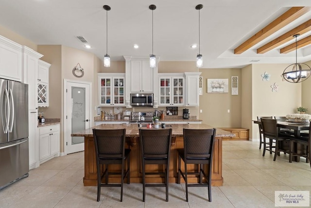 kitchen with pendant lighting, an island with sink, white cabinets, stainless steel appliances, and light stone countertops