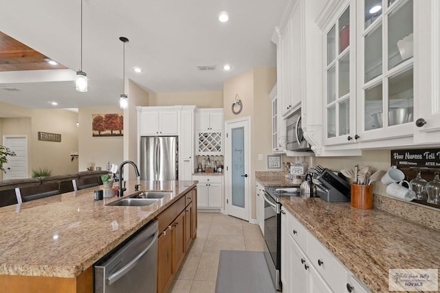 kitchen with appliances with stainless steel finishes, hanging light fixtures, light stone counters, white cabinets, and a center island with sink