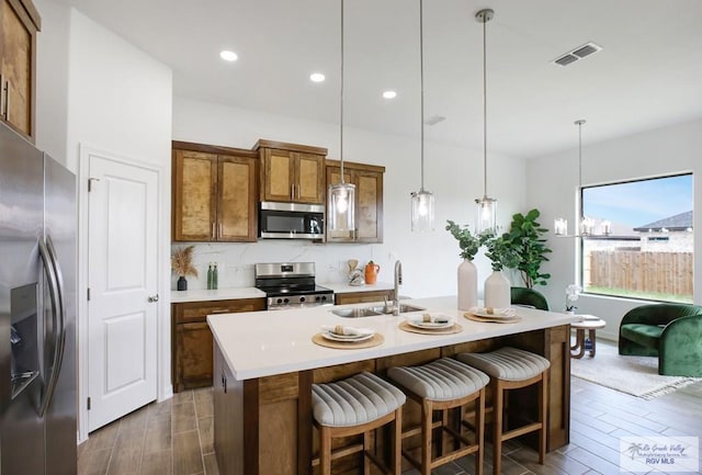 kitchen with a center island with sink, appliances with stainless steel finishes, sink, backsplash, and pendant lighting