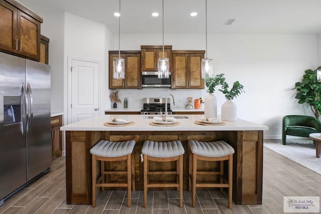 kitchen with a kitchen island with sink, hanging light fixtures, sink, appliances with stainless steel finishes, and a kitchen breakfast bar