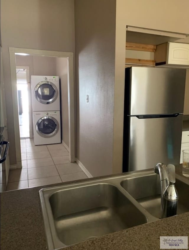 kitchen featuring light tile patterned flooring, stacked washer / dryer, sink, white cabinets, and stainless steel fridge