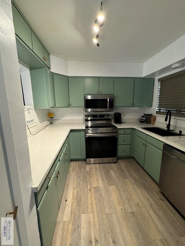 kitchen featuring appliances with stainless steel finishes, light wood-type flooring, green cabinets, and sink