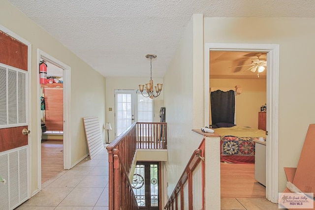 hall featuring a notable chandelier, light tile patterned floors, a textured ceiling, an upstairs landing, and baseboards