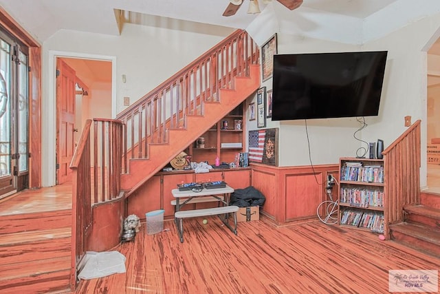 living room with arched walkways, a ceiling fan, wood finished floors, stairs, and built in shelves