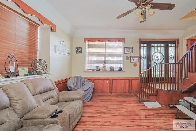 living room with a wainscoted wall, ceiling fan, light wood finished floors, and stairway