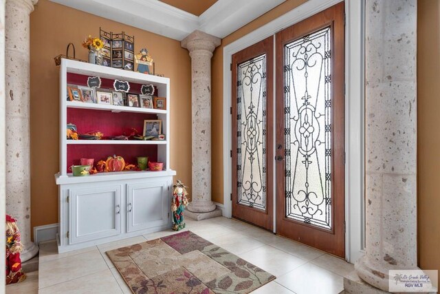 tiled foyer entrance with decorative columns, crown molding, and french doors